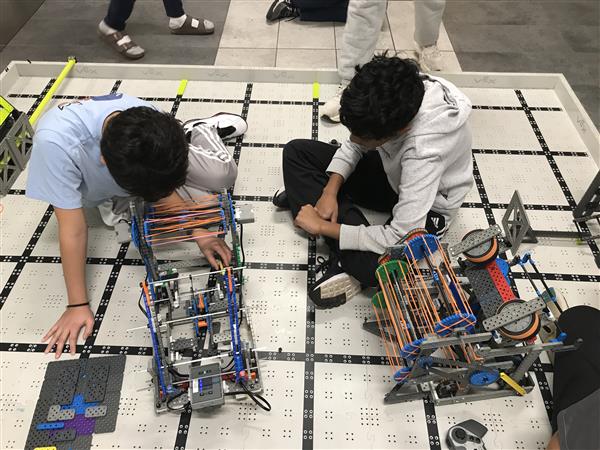 Students sit on a competition field with their robots at practice.